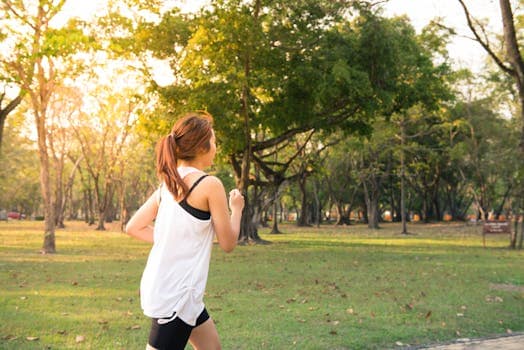 La Vitesse Maximale Aérobie (VMA) : clé de la performance en endurance A woman jogging through a forest park in the early morning sunshine, enjoying a healthy lifestyle.