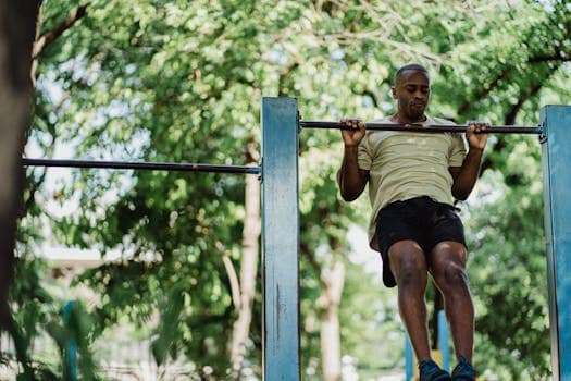 L'isométrie : une méthode d'entraînement redoutable pour tous les sportifs - partie 1 An athletic adult man doing a pull-up on an outdoor metal bar surrounded by green trees.