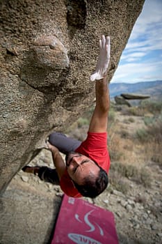 Services Man in red shirt bouldering on a steep rock face, showcasing strength and determination.