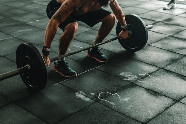 About A muscular man in a gym preparing to lift a heavy barbell, showcasing strength and fitness.